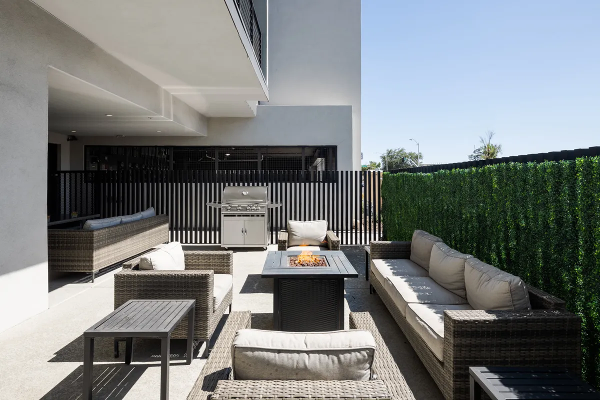 A cozy outdoor lounge area centered around a fire pit, with ample seating, a grill for barbecuing, and lush greenery all around. The scene is perfect for evening gatherings and relaxed socializing under the stars.