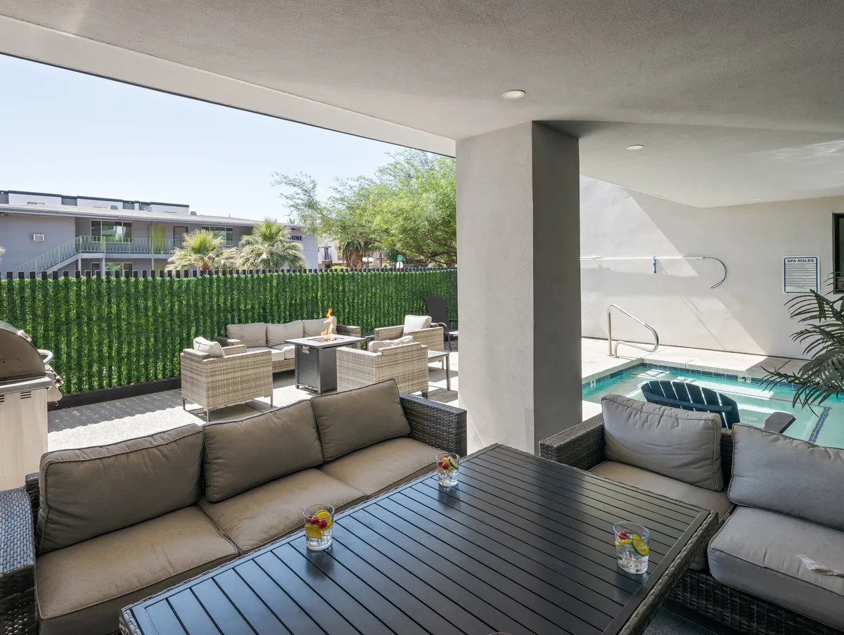 An inviting exterior view of an outdoor seating area beside a sparkling swimming pool, surrounded by greenery and a table with drinks. The space is clearly set up for relaxation, socializing, and outdoor fun.