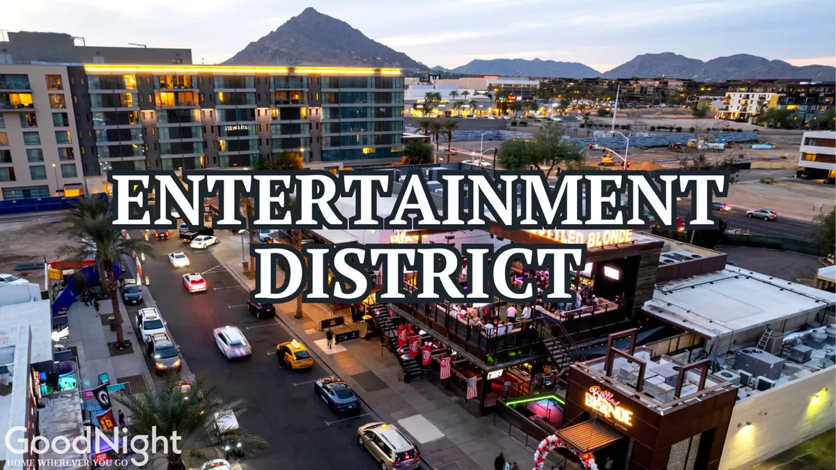 A vivid exterior shot of the Entertainment District, with the district's signage overhead, a lively street below, and a rooftop bar in the background. Cars and people hint at the area's excitement and nightlife activity.