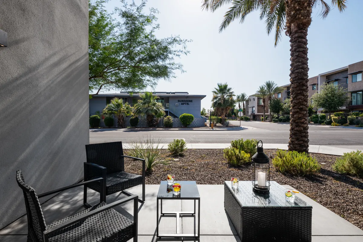 A welcoming patio scene with comfortable seating, palm trees, and a lantern, suggesting a casual setting for relaxing outdoors with friends or colleagues. The area is ideal for enjoying a drink or simply taking in the sunshine.