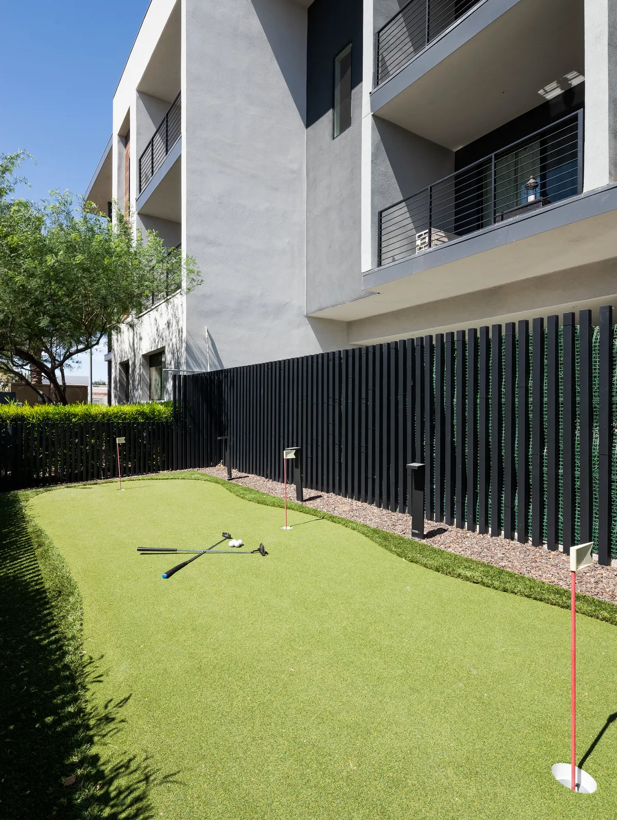 A modern exterior scene featuring a putting green in front of a stylish clubhouse facade. Golf clubs are visible, and the area is bathed in soft sunset light, creating a welcoming and recreational vibe.