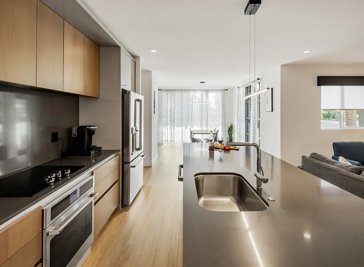 A bright, welcoming kitchen centered on a spacious island with bar seating and gleaming stainless steel appliances. Sunlight pours in through generous windows, highlighting the island’s role as a hub for meal prep and social interaction.